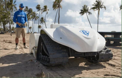 Operator walking behind the robot on a palm-lined beach